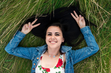 Happy girl lying on grass and showing peace by fingers.