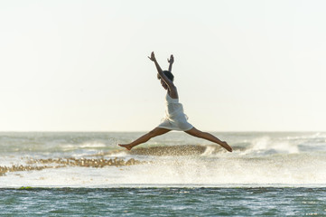 A beautiful young black woman leaps through the air as waves crash around her