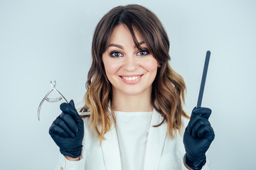 young attractive manicurist professional (master of manicure) woman in a white jacket and black rubber gloves is holds tools for removing cuticles and a nail file in a beauty spa salon