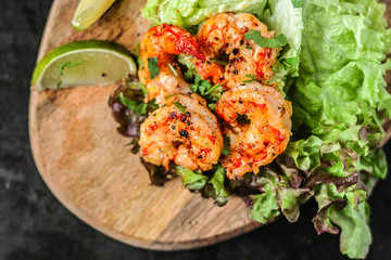 Roasted fried shrimps with green salad and lime on wood, top view