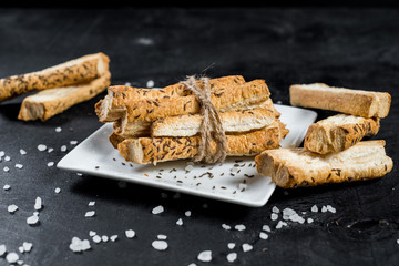 Tasty bread sticks with cumin on black background