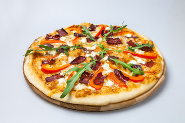appetizing pizza with bacon, cheese and pepper is decorated with arugula lays on the board