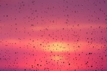 Drops of rain on a window glass against a background of a picturesque sky at sunset_