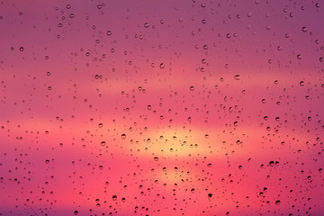 Drops of rain on a window glass against a background of a picturesque sky at sunset_