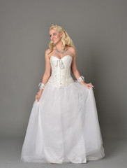 Fototapeta premium full length portrait of blonde girl wearing white corset gown. standing pose on grey studio background.