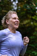 Close up of a female baby boomer in a purple top and black running pants on an evening run on a forest trail
