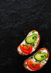 two slice of bread with cream cheese, cucumber, tomato on a black stone board. with copy space. top view