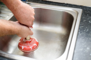 Man holding a plunger with two hands and no water in sink, used to clean a clogged / blocked...