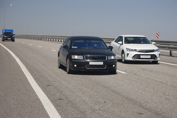 White and black sedans drive along the highway