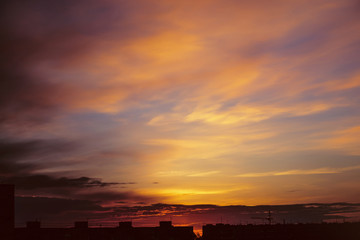 Beautiful cloudy dramatic morning sky above silhouette of city buildings. Picturesque dawn in city. Background of varicolored clouds. Unimaginable fantasy sunrise in heaven.