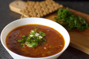 Lentil soup in a white bowl with bread and greens on a wooden board. Dinner. Lentil tomato soup with sour cream and herbs.