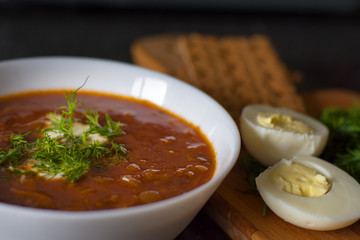 Lentil soup in a white bowl with bread, egg and greens on a wooden board. Dinner. Lentil tomato soup with sour cream and herbs.