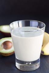 Healthy smoothie with avocado, banana, milk and honey on dark slate background, vertical, copy space