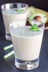 Healthy smoothie with avocado, banana, milk and honey on dark slate background, vertical