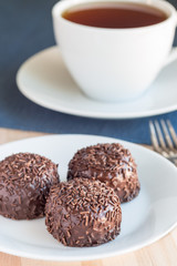 Swedish sweets Arrack balls, made from cookie crumbs, cocoa, butter and coconut wine Arrack flavour, on wooden table with cup of tea, vertical