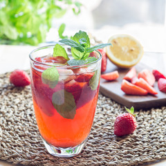 Homemade iced tea with strawberries and mint on a wooden table, square