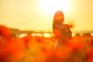 woman in a field with poppies at sunset, in the sun, soft focus