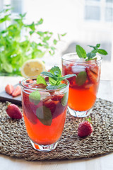 Homemade iced tea with strawberries and mint on wooden table, vertical