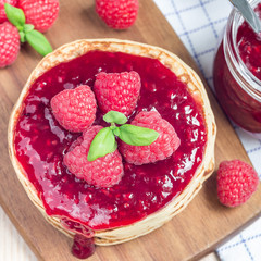 Stack of pancakes or fritters with raspberry jam and berries on wooden board, top view, square format