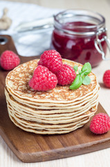 Stack of pancakes or fritters with raspberry on a wooden board, raspberry jam on background, vertical