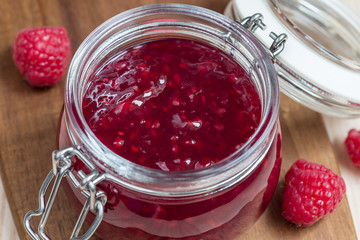 Raspberry jam in glass jar on wooden board, horizontal