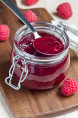 Raspberry jam in glass jar on a wooden board, vertical