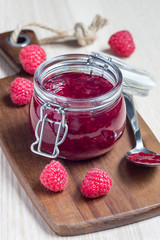 Raspberry jam in glass jar on wooden board, vertical