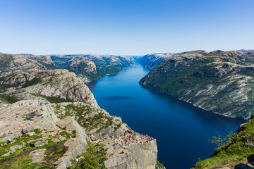 Naklejka na ściany i meble View at lysefjorden from above Preikestolen/Pulpit Rock in Norway with a clear blue sky. Lysefjorden, the Norwegian landscape and all the tourists standing at Preikestolen/Pulpit Rock.