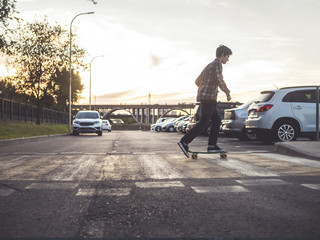 young hipster boy crossing the street riding the skateboard in the urban city