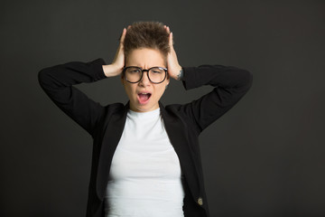 beautiful young girl with short hair, in a black suit and wearing glasses on a black background with a tired expression