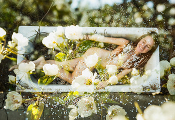 Bath in the nature. The smiling naked girl is washed by a flowering garden. An unusual shot. Art photo. - obrazy, fototapety, plakaty