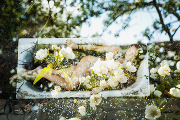 Lush flowering in the garden. Lush cherry blossoms cover the naked body of a smiling young girl, gracefully lying in the bath in the garden. - obrazy, fototapety, plakaty