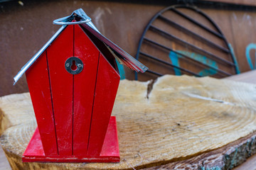 Tiny red house, maybe a bird house standing on a piece of wood with a old rusty cooking grid in the background. Seemed like leftovers from a garage sale turned into bulky waste.