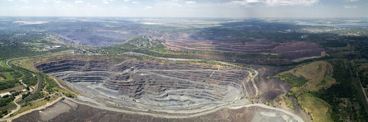 Aerial panoramic view of opencast mining quarry with lots of machinery at work.