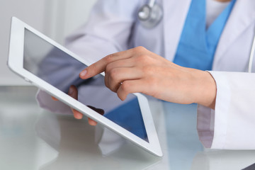 Female doctor using tablet computer while sitting at the workplace, close-up of hands. Medicine,...