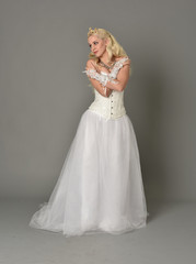 full length portrait of blonde girl wearing white corset gown. standing pose on grey studio background.