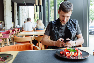 Portrait of a beautiful husband who has breakfast in a restaurant and looks into the phone