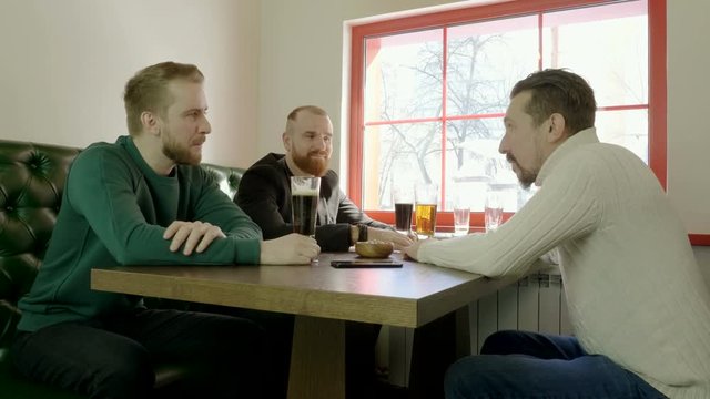 Meeting of friends. Three handsome men talking, laughing, drinking some beer in a restaurant. 4K
