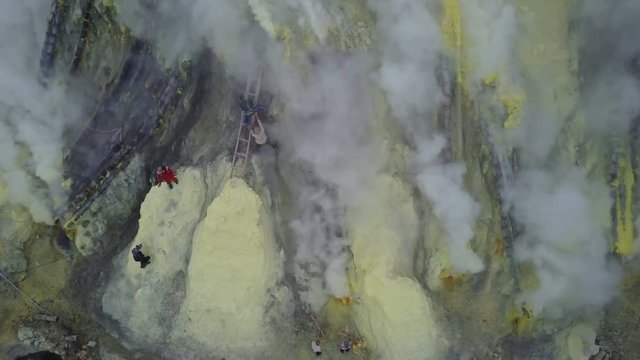 Smoke billows from hazardous sulfur mines, people working in tough conditions at Kawah Ijen volcanic crater lake in East Java, Indonesia