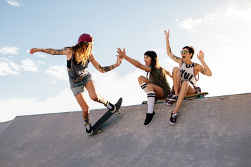 Skater girl riding skateboard at skate park with friends - obrazy, fototapety, plakaty