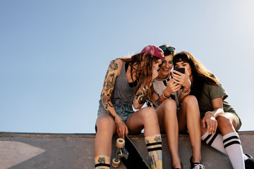 Female skaters sitting at skate park using smartphone