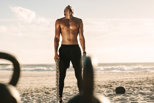 Man working out at the beach using battling rope and kettlebells