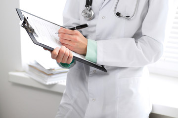Female doctor filling up medical form on clipboard closeup.  Healthcare, insurance and medicine concept