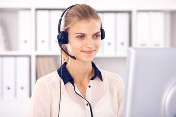 Call center operator. Blonde business woman in a headset in white office with pc computer