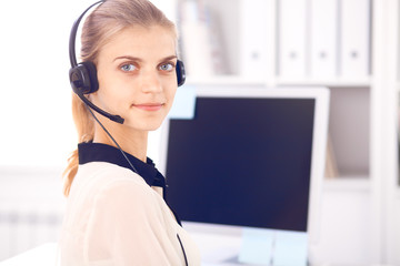 Call center operator. Blonde business woman in a headset in white office with pc computer