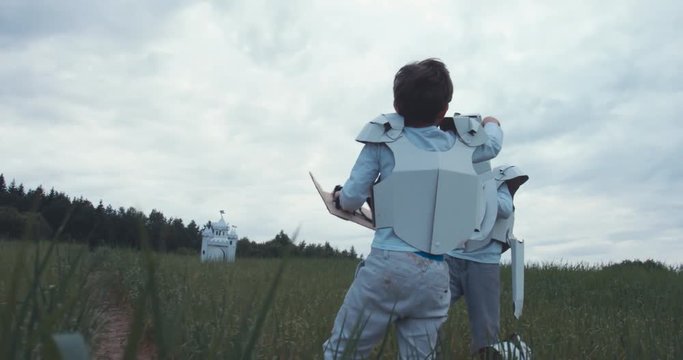 Brothers boys wearing handmade medieval knight armor costumes having a sword fight near cardboard castle. 4K UHD 60 FPS SLO MO
