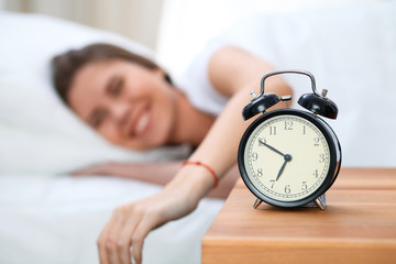 Sleepy young woman stretching hand to ringing alarm willing turn it off. Early wake up, not getting...