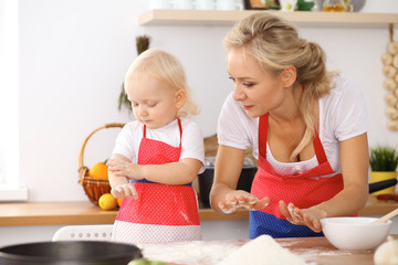 Little girl and her blonde mom in red aprons  playing and laughing while kneading the dough in the kitchen. Homemade pastry for bread, pizza or bake cookies