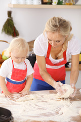 Little girl and her blonde mom in red aprons  playing and laughing while kneading the dough in the kitchen. Homemade pastry for bread, pizza or bake cookies