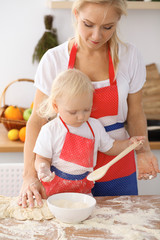 Little girl and her blonde mom in red aprons  playing and laughing while kneading the dough in the kitchen. Homemade pastry for bread, pizza or bake cookies